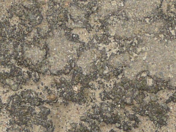 Grey asphalt texture covered with small broken areas of crumbling rock and sandy soil.